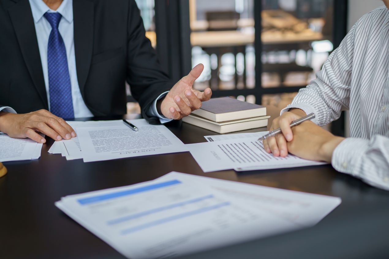 Arbeitnehmer und Anwalt besprechen eine Kündigungsschutzklage am Schreibtisch. Wichtige Dokumente und Verträge liegen auf dem Tisch.